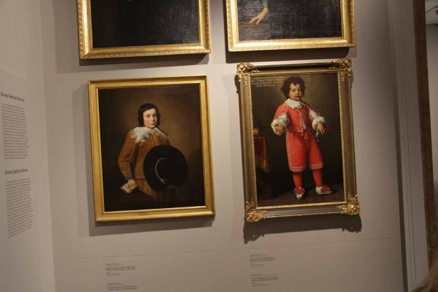 Zwei Porträtgemälde von Kindern in historischen Kostümen hängen an einer Wand.