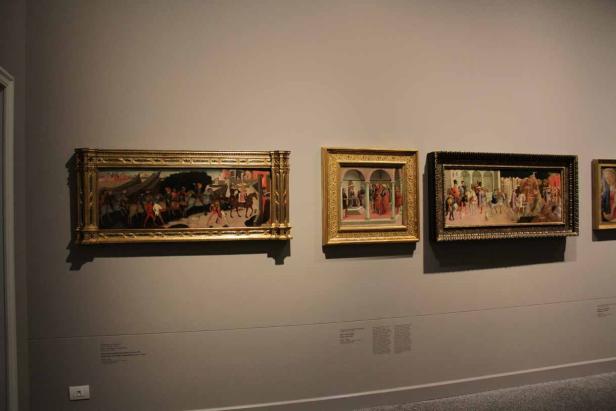 Mehrere gerahmte Gemälde hängen an einer grauen Wand in einem Museum.
