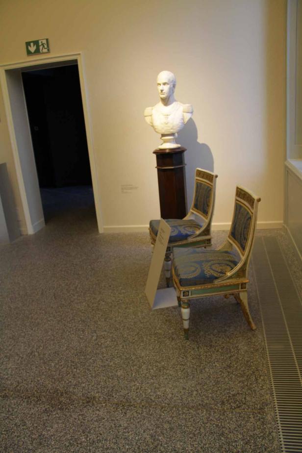 In einem Museum stehen zwei Stühle vor einer Büste.