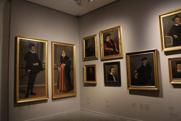 In einem Museum hängen mehrere Porträtgemälde an einer grauen Wand.