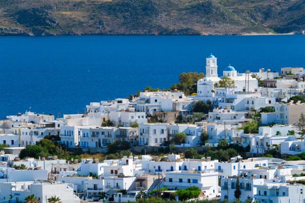 Blick auf eine griechische Insel mit weiß getünchten Häusern und einer Kirche mit blauen Kuppeln.