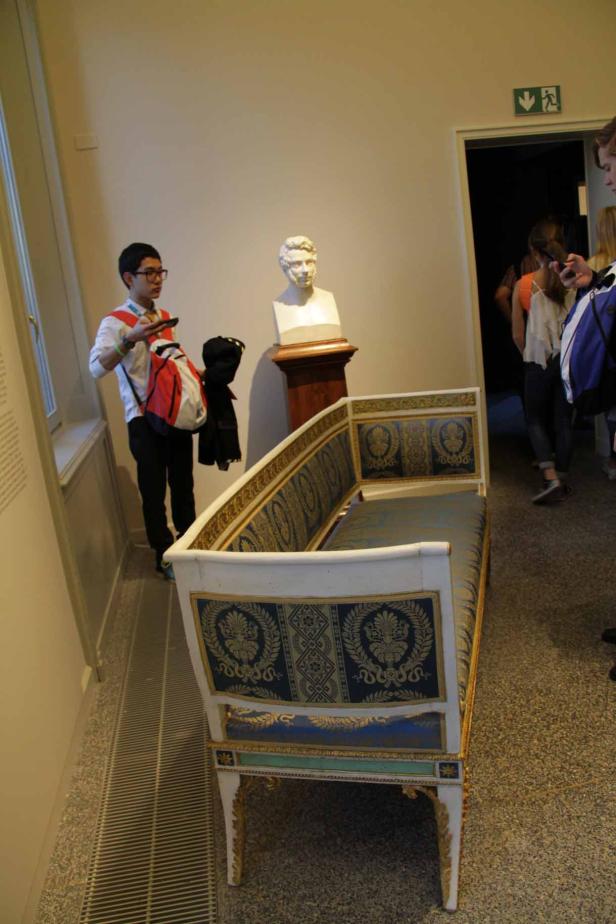 Ein Museumsbesucher betrachtet eine antike Bank und eine Büste.