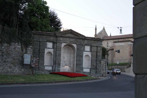 Ein steinernes Bauwerk mit roten Blumen an einer Straßenecke.
