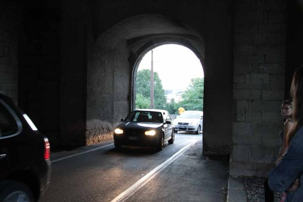 Ein dunkler VW Golf fährt durch einen steinernen Torbogen.