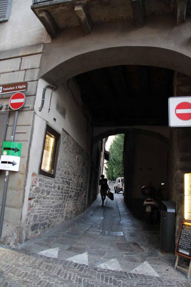 Eine Frau geht durch einen schmalen, gewölbten Durchgang in einer italienischen Stadt.