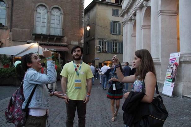 Zwei Frauen fotografieren einen Mann mit Namensschild in einer belebten Stadtstraße.