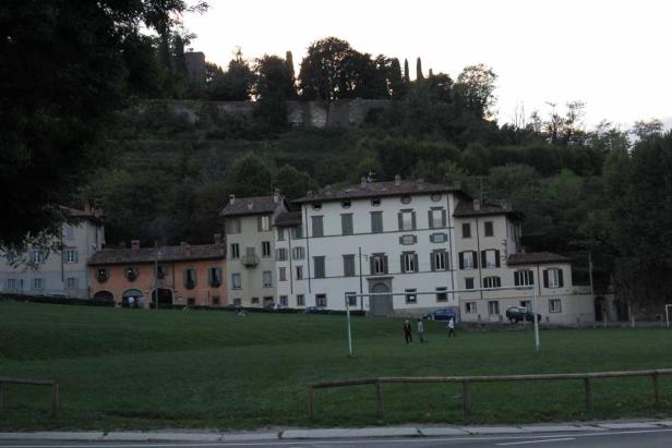 Mehrere Gebäude stehen an einem Hang mit Bäumen und einer Wiese.