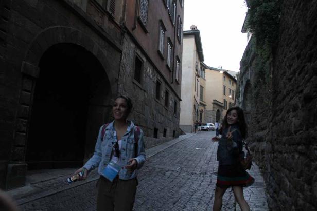 Zwei junge Frauen spazieren eine Kopfsteinpflasterstraße entlang.