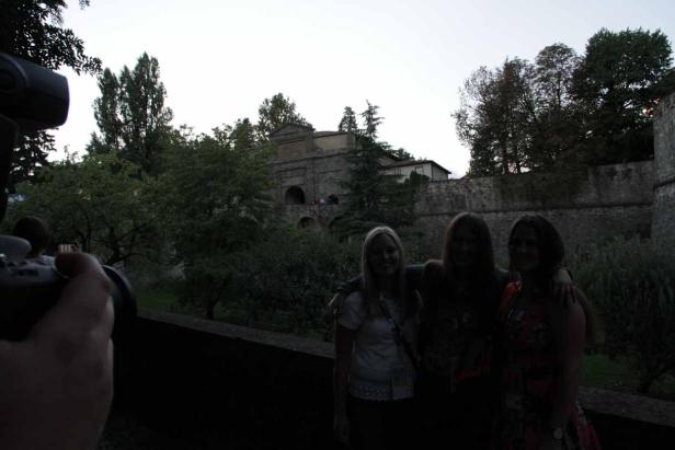 Drei Frauen posieren vor einer alten Steinmauer und einem Torbogen.