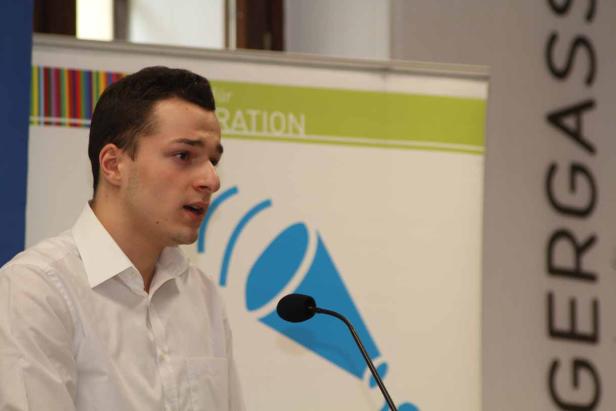 Ein junger Mann spricht bei einer Veranstaltung am Rednerpult.