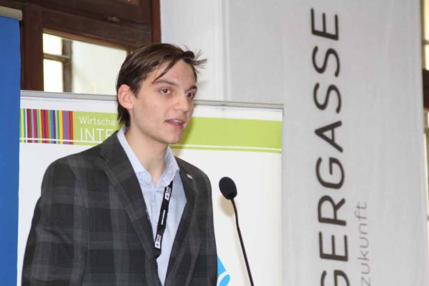 Ein junger Mann spricht an einem Mikrofon vor einem Banner der Wirtschaftskammer.