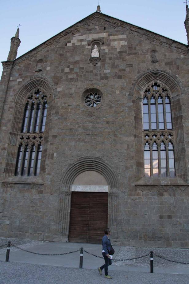 Eine Frau geht vor einer alten Steinkirche mit gotischen Fenstern entlang.