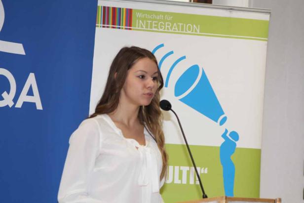 Eine junge Frau spricht an einem Rednerpult vor einem Banner „Wirtschaft für Integration“.