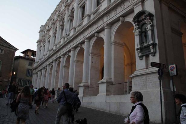 Menschen gehen an einem Gebäude mit Säulengang vorbei.