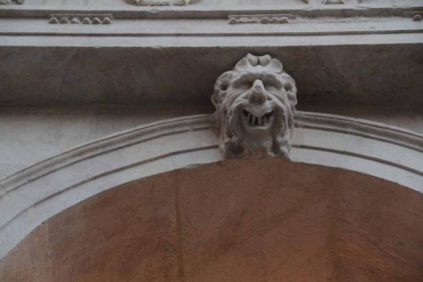 Eine steinerne Fratze ziert den Bogen eines Gebäudes.
