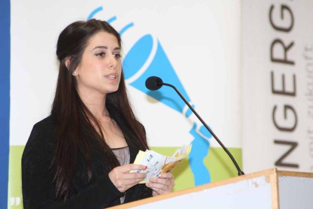 Eine junge Frau hält eine Rede an einem Rednerpult mit Mikrofon.