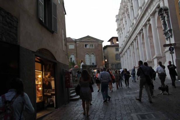 Menschen gehen eine Kopfsteinpflasterstraße in einer italienischen Stadt entlang.