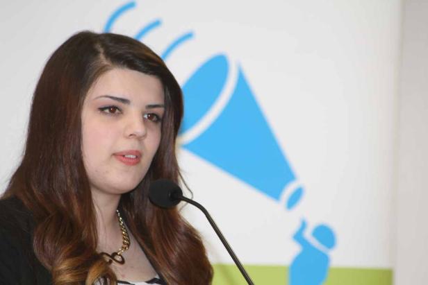 Eine junge Frau spricht am Rednerpult vor einem blauen Logo.