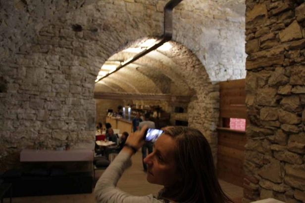 Eine Frau fotografiert mit ihrem Smartphone in einem Restaurant mit Steingewölbe.