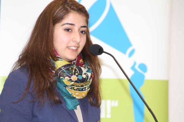 Eine junge Frau spricht bei einer Veranstaltung in ein Mikrofon.