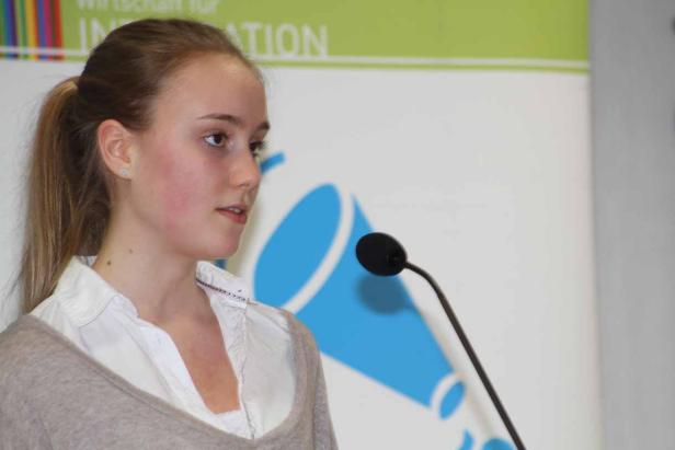 Eine junge Frau spricht an einem Mikrofon vor einem Banner.