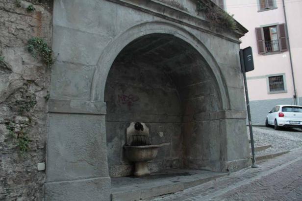 Ein alter, steinerner Brunnen steht an einer Straße.