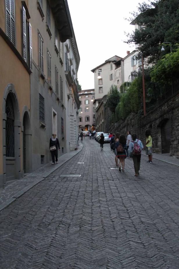 Eine Gruppe von Menschen geht eine Kopfsteinpflasterstraße in einer italienischen Stadt entlang.