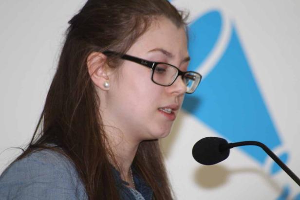 Eine junge Frau mit Brille spricht in ein Mikrofon.