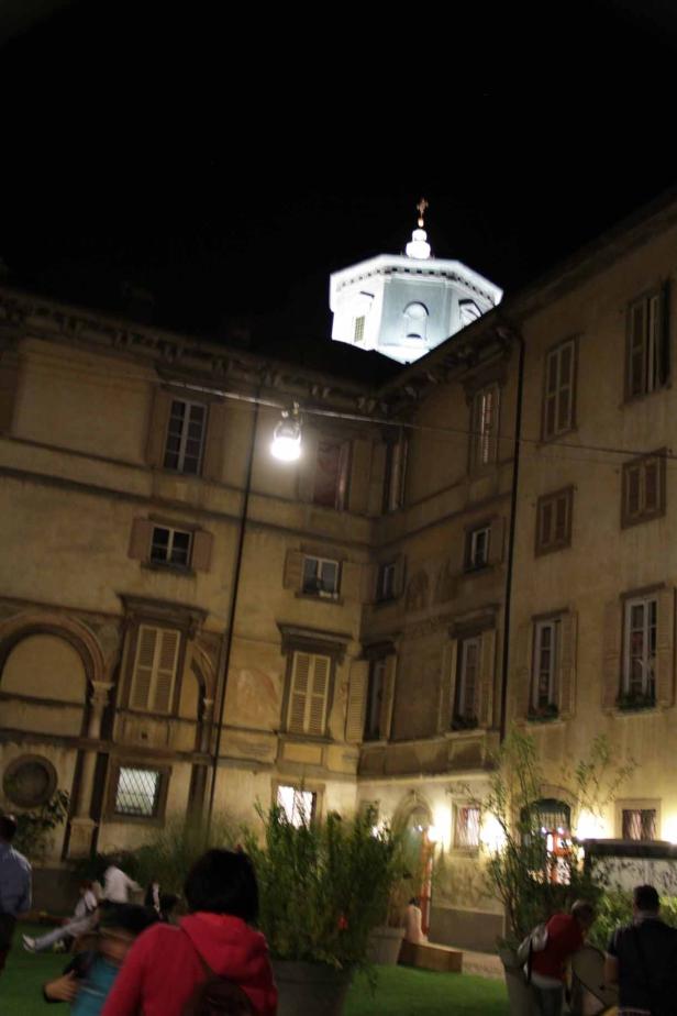 Ein beleuchteter Innenhof mit einem Kuppelbau im Hintergrund bei Nacht.