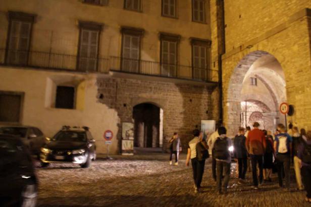 Eine Gruppe von Menschen geht nachts durch einen Torbogen in einer Stadt.