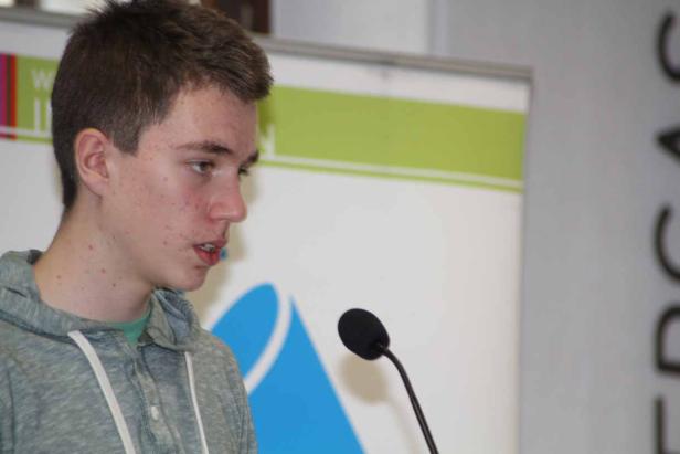 Ein junger Mann spricht in ein Mikrofon vor einem Banner.