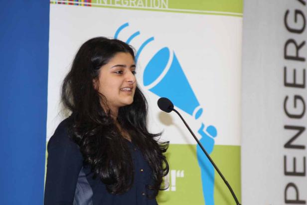 Eine junge Frau spricht bei einer Veranstaltung am Mikrofon.