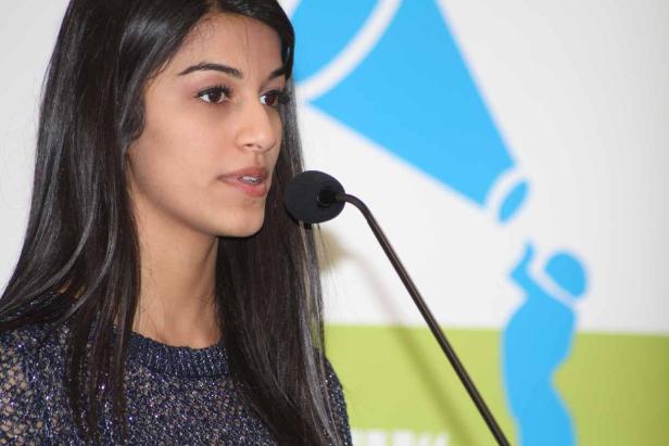 Eine junge Frau spricht bei einer Veranstaltung in ein Mikrofon.