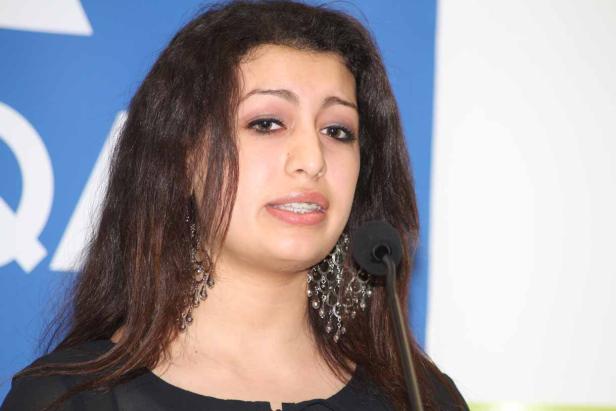 Eine Frau mit dunklen Haaren spricht in ein Mikrofon.