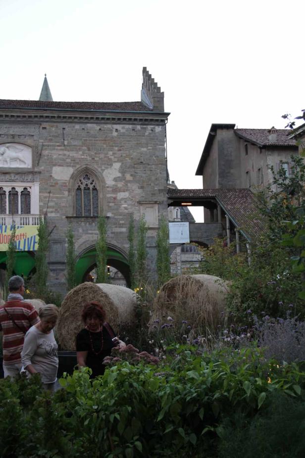 Menschen stehen vor Heuballen und Blumen in der Nähe eines alten Gebäudes.