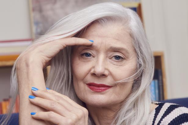 Eine Frau mit grauen Haaren und blau lackierten Fingernägeln blickt in die Kamera.