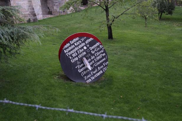 Eine runde Installation mit Text und Symbolen steht auf einer Rasenfläche.