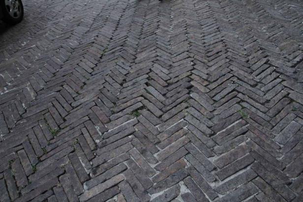 Ein Gehweg ist mit Ziegelsteinen in einem Fischgrätenmuster gepflastert.