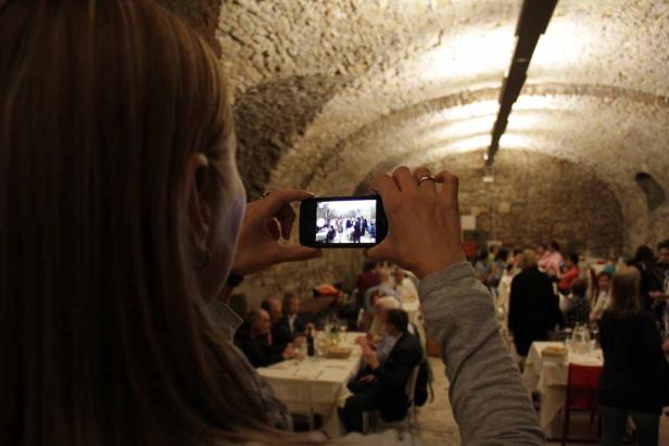 Eine Frau fotografiert mit ihrem Smartphone eine Gruppe von Menschen in einem Gewölbekeller.