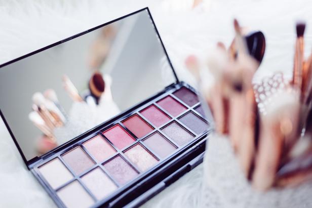 Eine geöffnete Lidschattenpalette mit verschiedenen Rosa- und Brauntönen liegt neben Make-up-Pinsel auf einem weichen Untergrund.