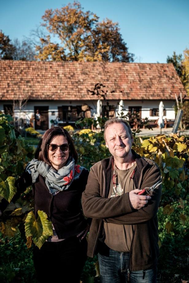 Ein Mann mit einer Gartenschere und eine Frau stehen vor einem Haus mit einem Weinberg.