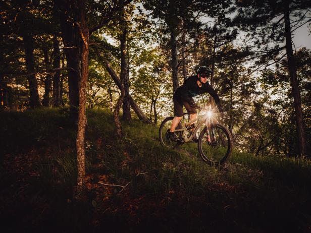 Ein Mountainbiker fährt mit eingeschaltetem Scheinwerfer durch einen Wald.
