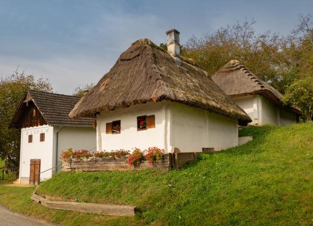 Mehrere traditionelle Bauernhäuser mit Strohdächern auf einem grünen Hügel.