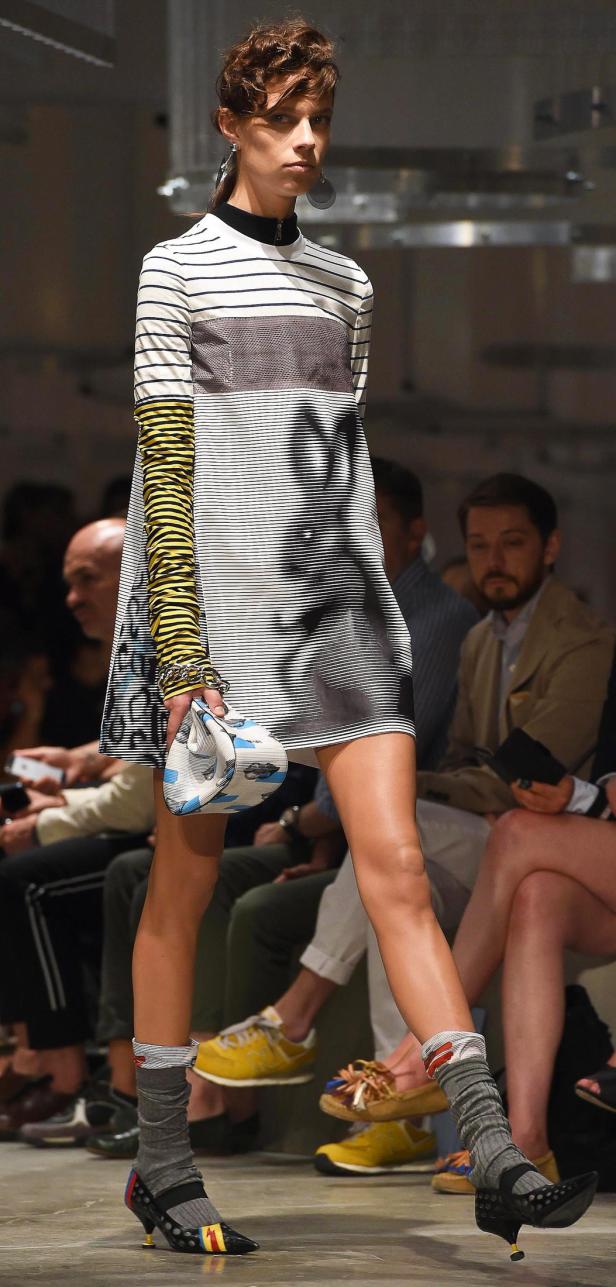 Eine Frau präsentiert ein gestreiftes Minikleid und auffällige Accessoires auf dem Laufsteg.