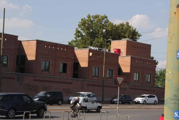 Ein Radfahrer fährt an einer Straße mit parkenden Autos und einem Backsteingebäude entlang.