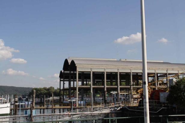 Ein großes, offenes Gebäude am Wasser unter einem blauen Himmel.