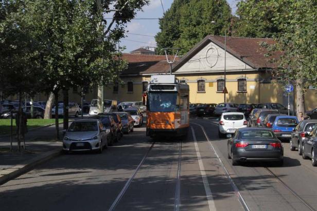 Eine orangefarbene Straßenbahn fährt auf einer Straße mit parkenden Autos.