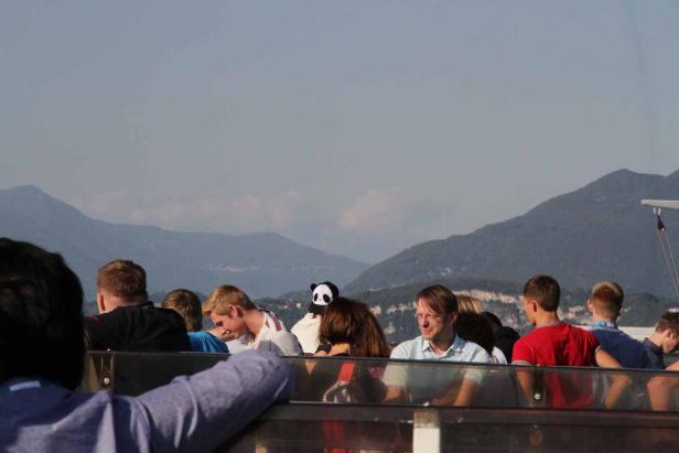 Eine Gruppe von Menschen sitzt vor einer Bergkulisse, eine Person trägt einen Panda-Hut.