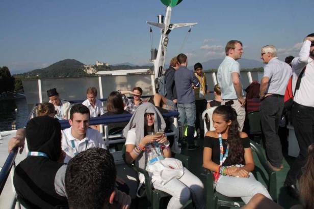 Eine Gruppe von Menschen genießt eine Bootsfahrt auf einem See mit Blick auf eine Burg im Hintergrund.