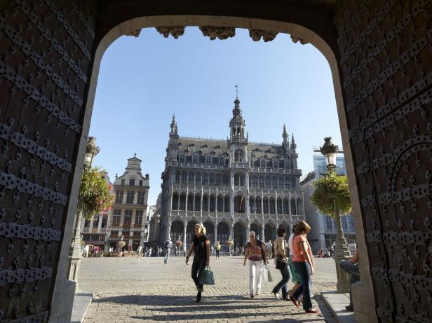 Blick durch ein Tor auf den Grand Place in Brüssel mit Passanten.